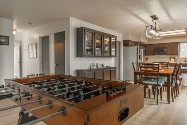 Finished basement recreation room with foosball table, dining area, and kitchen in background