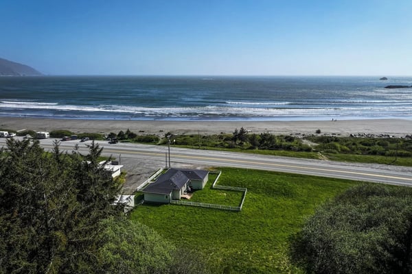 Coastal house with fenced yard on grassy bluff overlooking sandy beach and ocean waves